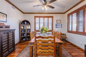 A dining room with a wooden table, chairs, a ceiling fan, and a decorative cabinet.