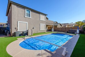 A residential backyard with a swimming pool, a covered patio, and a lawn.