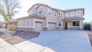A two-story house with a stone foundation, multiple garage doors, and a driveway leading to a gated entrance. - Relax in Home w/ Htd. Pool+Hot Tub,  Putting Green, Whirlpool Bath+Steam Shower (Queen Creek)