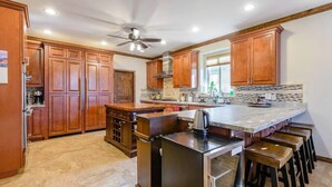 A spacious kitchen with wooden cabinets, a central island with stools, a built-in oven, and a ceiling fan. - Relax in Home w/ Htd. Pool+Hot Tub,  Putting Green, Whirlpool Bath+Steam Shower (Queen Creek)