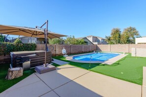 A backyard with a swimming pool, a hot tub, and a barbecue area.