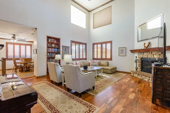 A spacious living room with hardwood floors, a fireplace, a bookshelf, and a dining area with wooden furniture.
