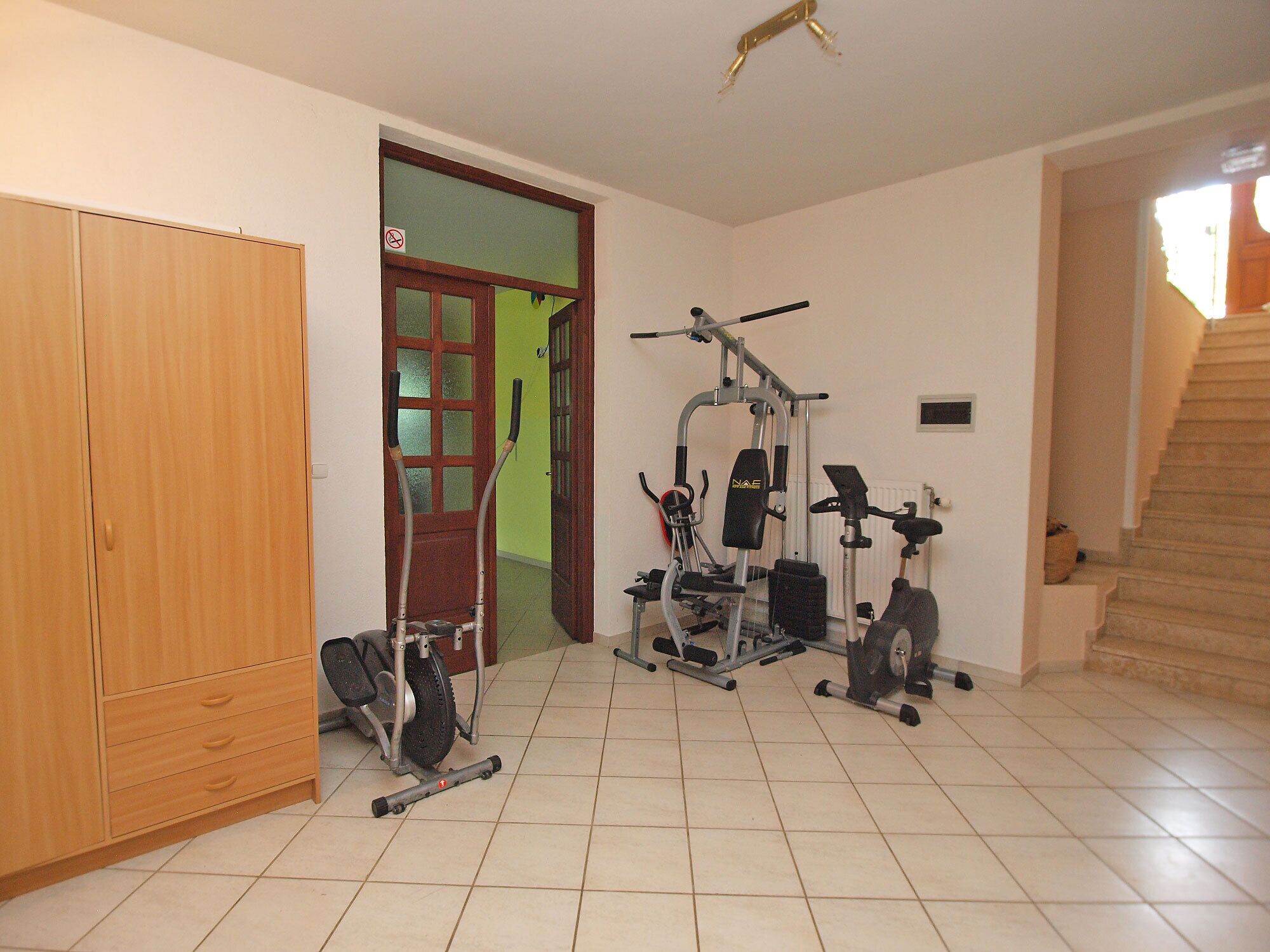 Une salle de sport à domicile équipée de matériel d’exercice, une armoire en bois et un escalier.