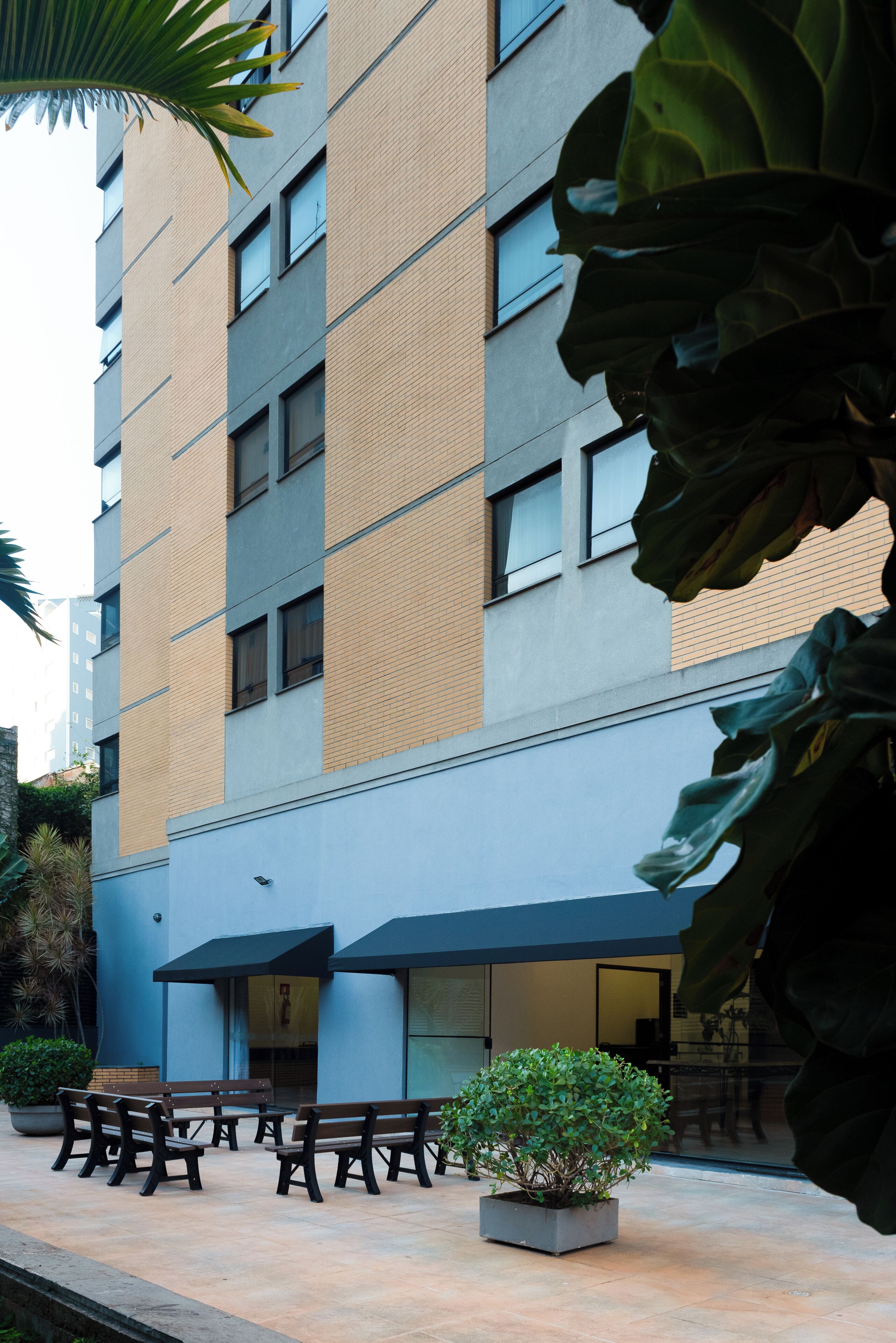 A modern building with a mix of brick and concrete exterior, large windows, and a small outdoor seating area with benches and a potted plant.