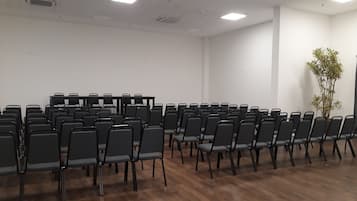 Un salón de conferencias con filas de sillas, una mesa y una planta en maceta.