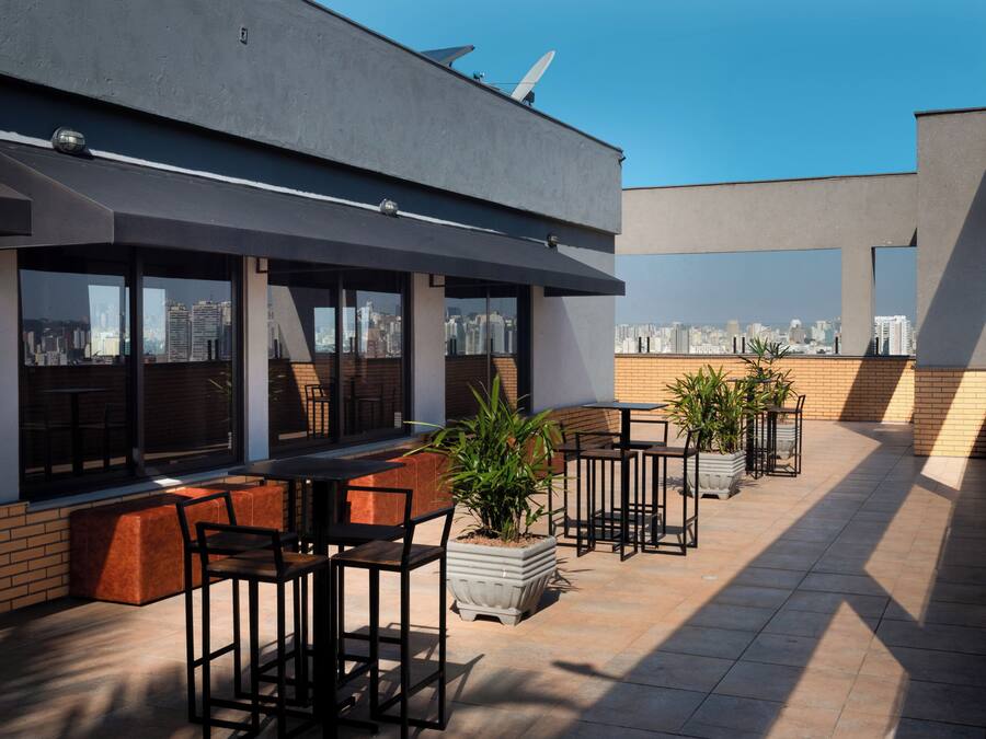 Eine Dachterrasse mit Sitzgelegenheiten im Freien, Blumentöpfen und Blick auf die Stadt.