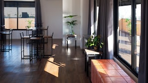 A spacious room with a wooden floor, a dining area with chairs and a table, a bench, and large windows with curtains. - Intercity São Paulo Anhembi (São Paulo)