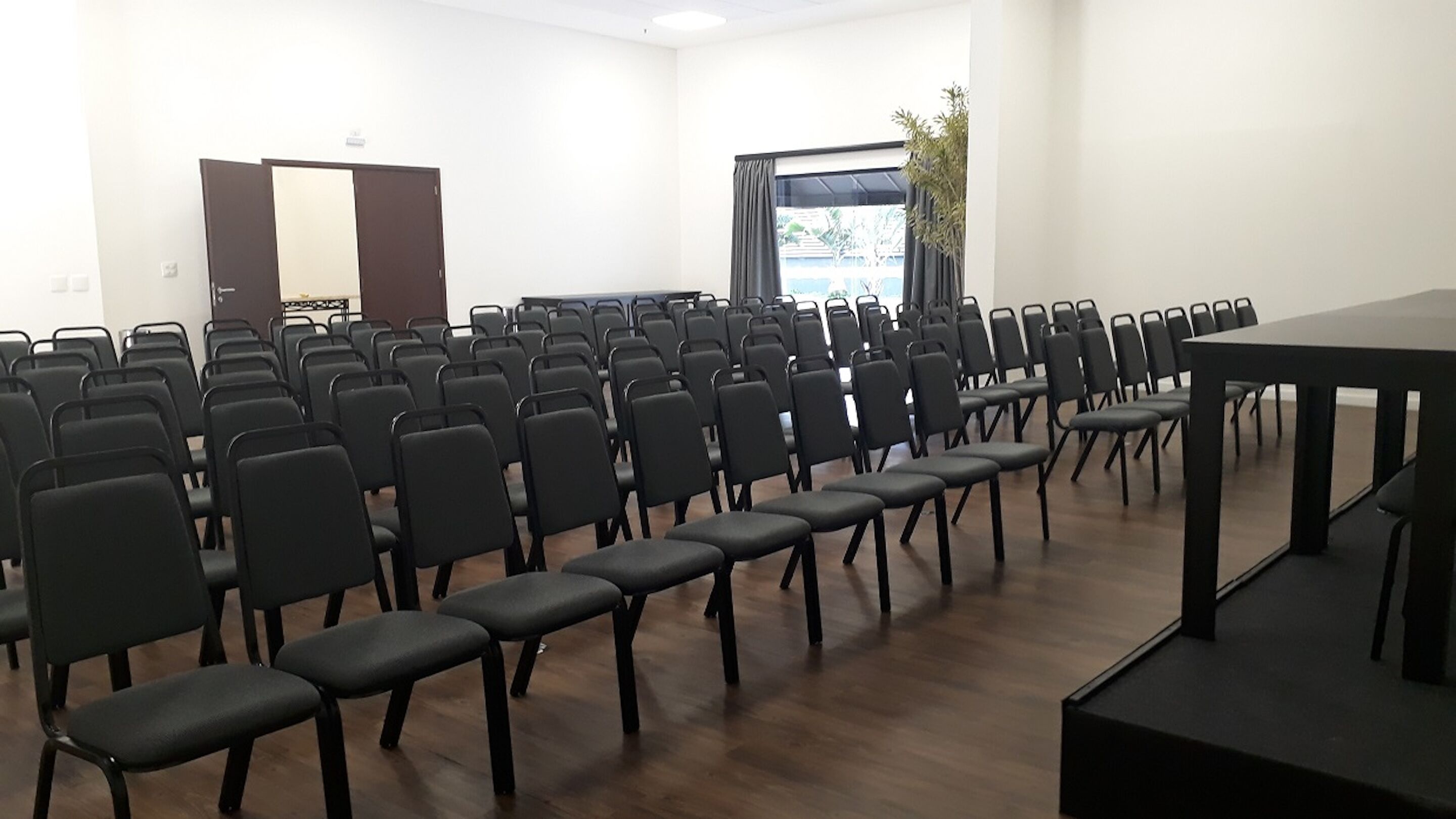A conference room with rows of black chairs, a large table, and a door in the background.