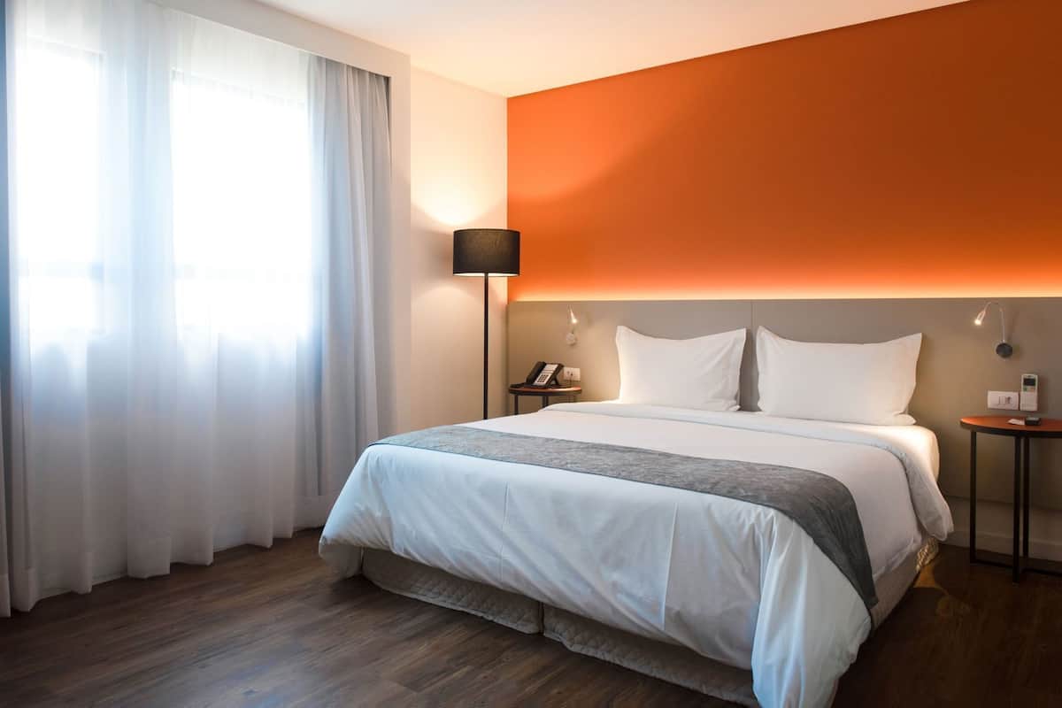 Ein Hotelzimmer mit Bett, Nachttisch, Lampe und Blick ins Freie.