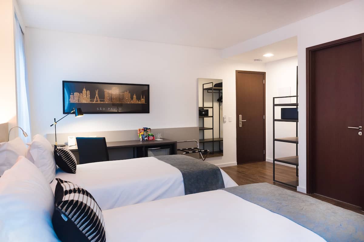 Ein Hotelzimmer mit zwei Betten, einem Schreibtisch, einem Stuhl, einem Spiegel und einer Tür.