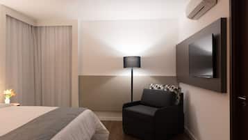 A hotel room with a bed, a chair, a TV mounted on the wall, and a lamp.