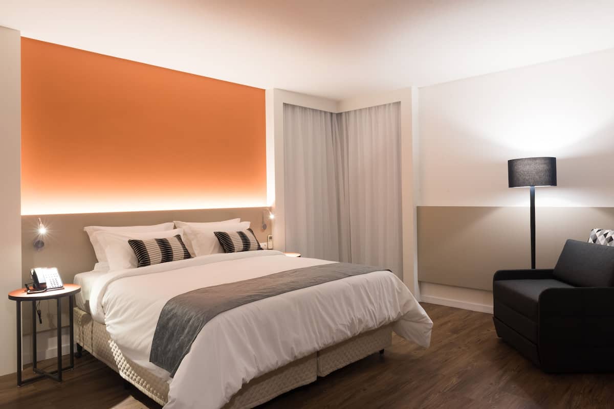 Ein Hotelzimmer mit Bett, Nachttisch, Lampe und einem Sessel.