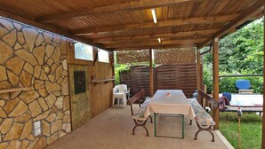 Une terrasse extérieure avec un mur en pierre, un plafond en bois et une table entourée de chaises.