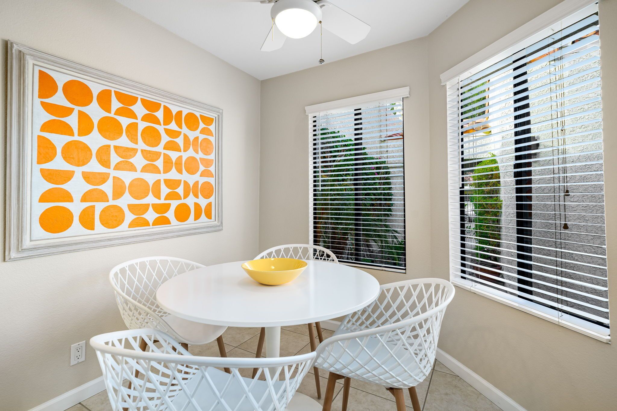 A dining area with a white table and chairs, a yellow bowl, and a ceiling fan.