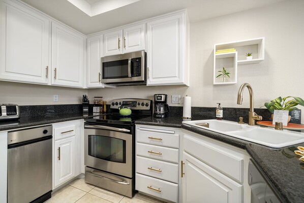 A modern kitchen with white cabinets, stainless steel appliances, a black countertop, and a built-in microwave.