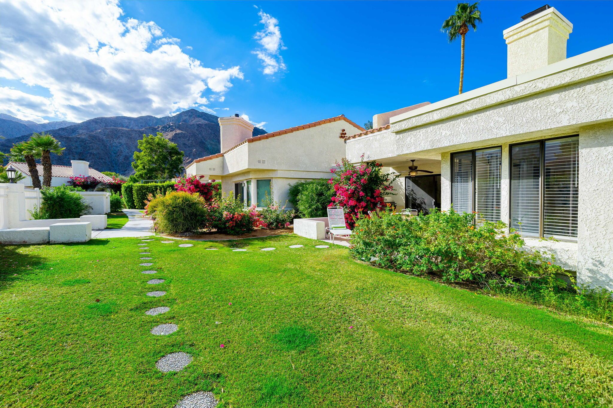 A modern house with a well-maintained lawn, a patio area, and a mountain backdrop.
