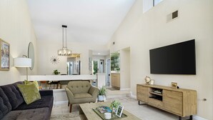Een moderne woonkamer met een bank, fauteuil, salontafel en een aan de muur bevestigde televisie.