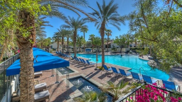 Un espace piscine agrémenté de chaises longues et de parasols, entouré de palmiers et surplombé d’un ciel bleu azur.