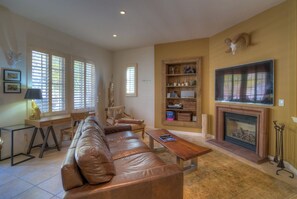 A living room with a leather sofa, a coffee table, a fireplace, and a bookshelf.