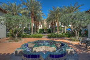 A courtyard with palm trees, a tiled fountain, and a seating area.