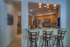 A kitchen with wooden cabinets, a granite countertop, and a central island with bar stools.