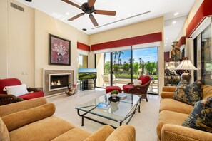 A spacious living room with a fireplace, comfortable seating, a glass coffee table, and a view of the outdoors.