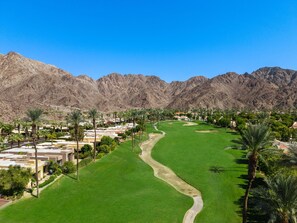 A golf course with a clear path, surrounded by palm trees and buildings, with mountains in the background.