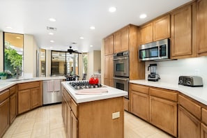 A modern kitchen with wooden cabinets, stainless steel appliances, and a central island with a gas stove.