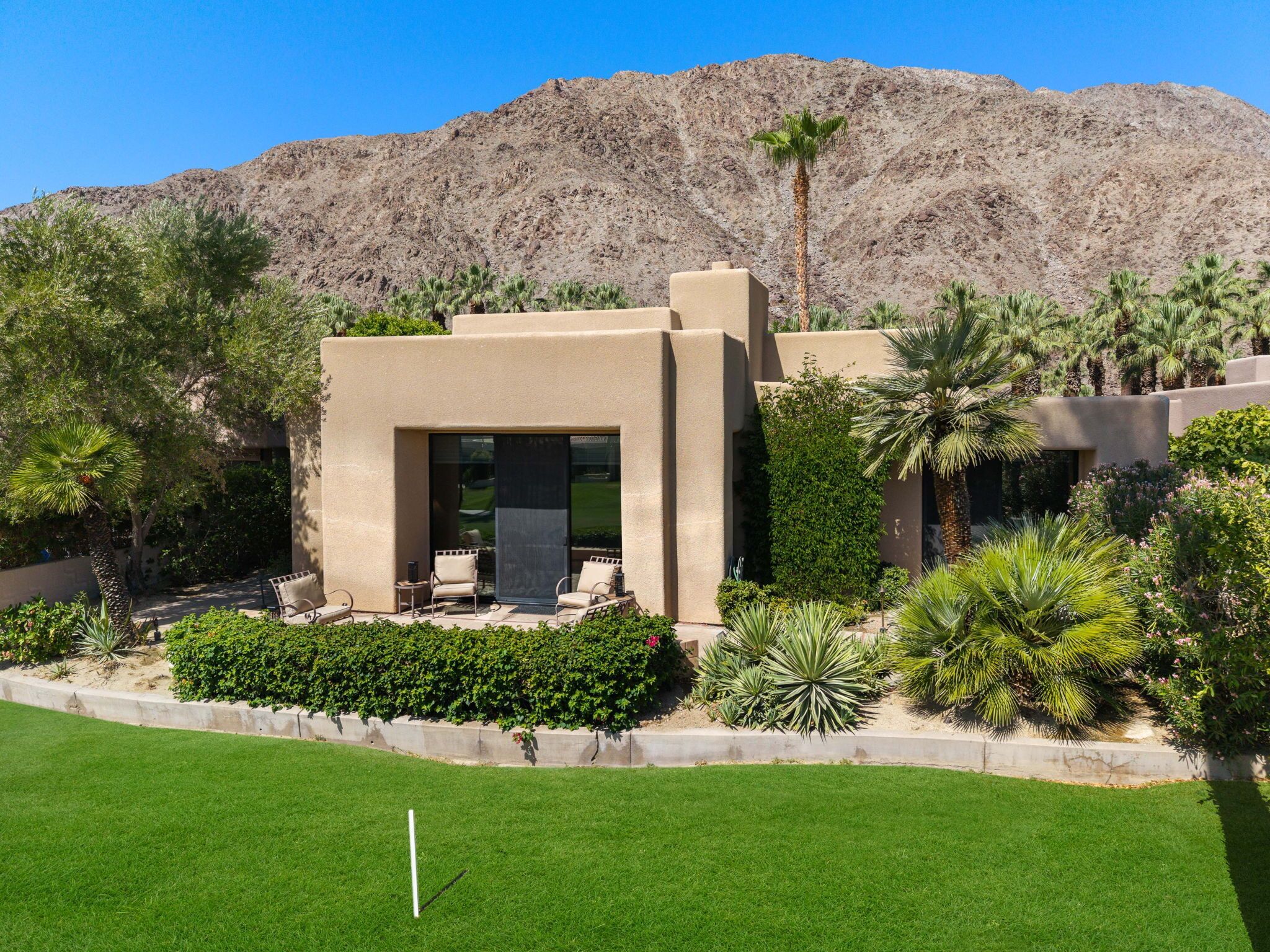 A modern building with a patio area, surrounded by landscaped gardens and palm trees.