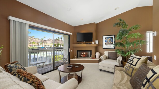 A living room with a fireplace, a television, and a balcony with a view of mountains. - Tennis Villa #3 - Courtside View, 2 bed, 2 bath, Permit 067145 (La Quinta)
