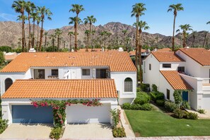 A residential area with white houses featuring red-tiled roofs, surrounded by palm trees and mountains in the background. - Tennis Villa #3 - Courtside View, 2 bed, 2 bath, Permit 067145 (La Quinta)