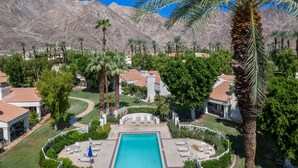 An aerial view of a resort with a central swimming pool, surrounded by palm trees and houses with red-tiled roofs. - Tennis Villa #3 - Courtside View, 2 bed, 2 bath, Permit 067145 (La Quinta)