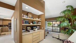 A modern kitchen with built-in appliances, a dining area with a large window, and a living room with a sofa and a potted plant. - Tennis Villa #3 - Courtside View, 2 bed, 2 bath, Permit 067145 (La Quinta)