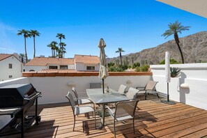 A patio with a grill, table, and chairs, overlooking palm trees and a mountain. - Tennis Villa #3 - Courtside View, 2 bed, 2 bath, Permit 067145 (La Quinta)