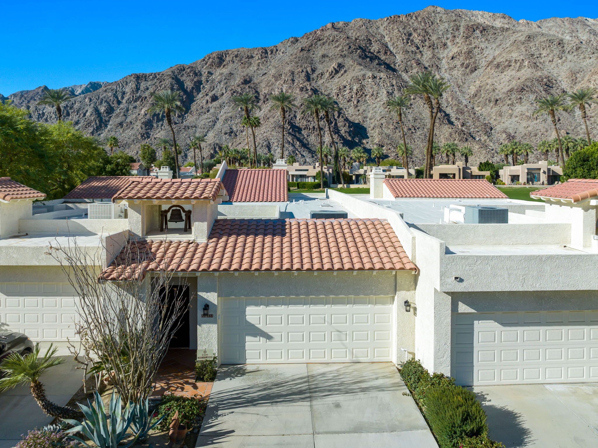 A residential area with houses featuring red-tiled roofs, white garage doors, and a mountainous backdrop.