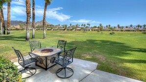 A patio with a round table and chairs, surrounded by palm trees and a view of a residential area. - Duna La Quinta #2 - Fairway Home - Pet Friendly (La Quinta)