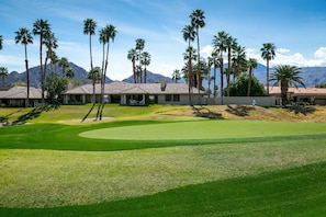 Un parcours de golf doté d’un club-house, de palmiers et avec des montagnes en toile de fond.