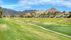 A golf course with a clear path, surrounded by houses and palm trees, with mountains in the background. - Duna La Quinta #2 - Fairway Home - Pet Friendly (La Quinta)
