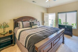 A bedroom with a large bed, a nightstand, a dresser, and a window with a view of greenery. - Duna La Quinta #2 - Fairway Home - Pet Friendly (La Quinta)