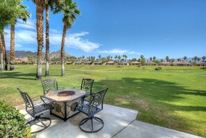 A patio with a round table and chairs, surrounded by palm trees and a view of a residential area. - Duna La Quinta #2 - Fairway Home - Pet Friendly (La Quinta)