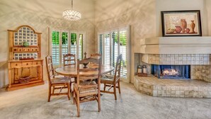 A dining area with a round wooden table and chairs, a hanging light fixture, a fireplace, and a decorative cabinet. - Santa Rosa Cove #16 - Greenbelt, 3 bedroom/3.5 bath, permit 063424 (La Quinta)