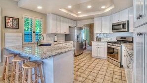 A modern kitchen with white cabinets, a granite countertop, stainless steel appliances, and a tiled floor. - Santa Rosa Cove #16 - Greenbelt, 3 bedroom/3.5 bath, permit 063424 (La Quinta)