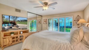 A bedroom with a large bed, a ceiling fan, a TV, and a view of a golf course through the windows. - Santa Rosa Cove #16 - Greenbelt, 3 bedroom/3.5 bath, permit 063424 (La Quinta)