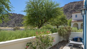 Un patio con una parrilla, un muro blanco y un árbol de flores rosadas.