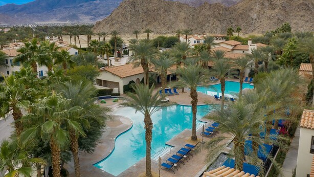 Un resort con piscina rodeada de palmeras y edificios con tejados rojos.