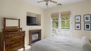 Un dormitorio con cama, cómoda, televisión, chimenea, ventilador de techo y ventana con vistas.