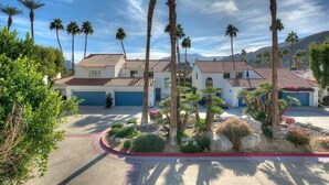 A two-story house with a red-tiled roof, surrounded by palm trees and a landscaped garden. - Tennis Villa - TV005 - Beautiful Mountain Views (La Quinta)