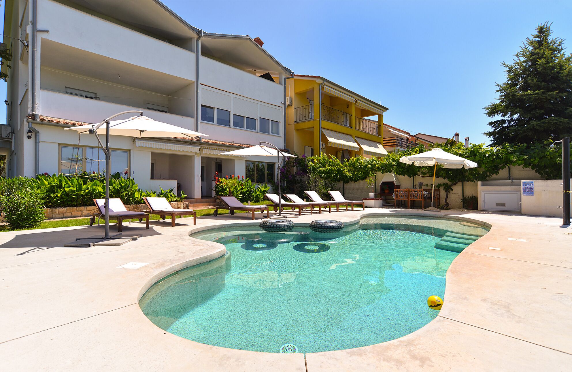 Uma piscina com espreguiçadeiras e guarda-sóis, cercada por edifícios com varandas e áreas de estar ao ar livre.