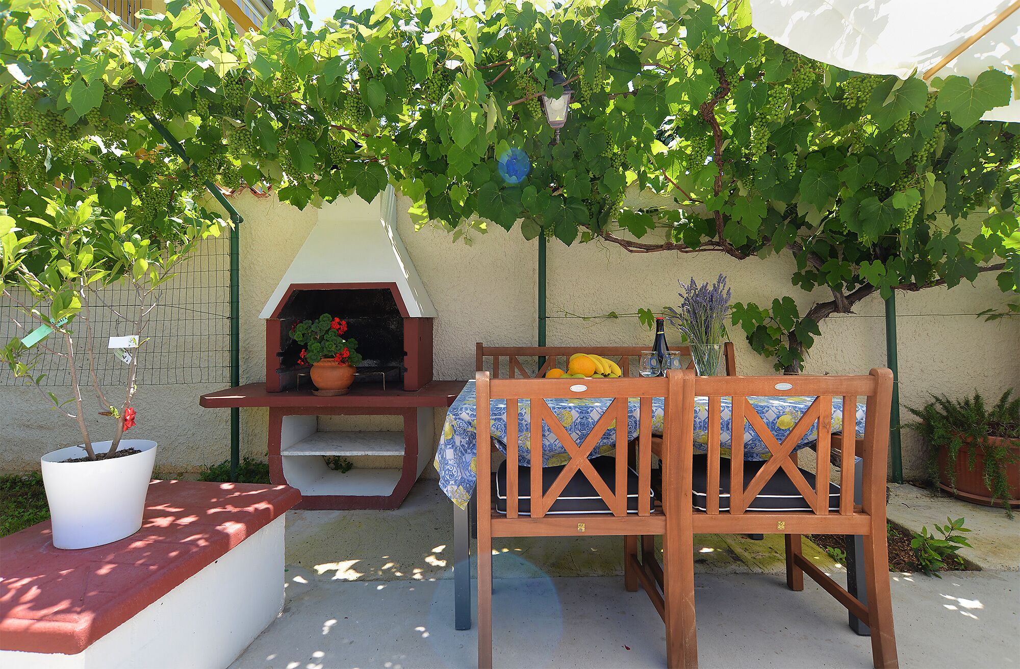 Eine Terrasse im Freien mit einem Holztisch und -stühlen, einem Grill und einem Blumentopf.