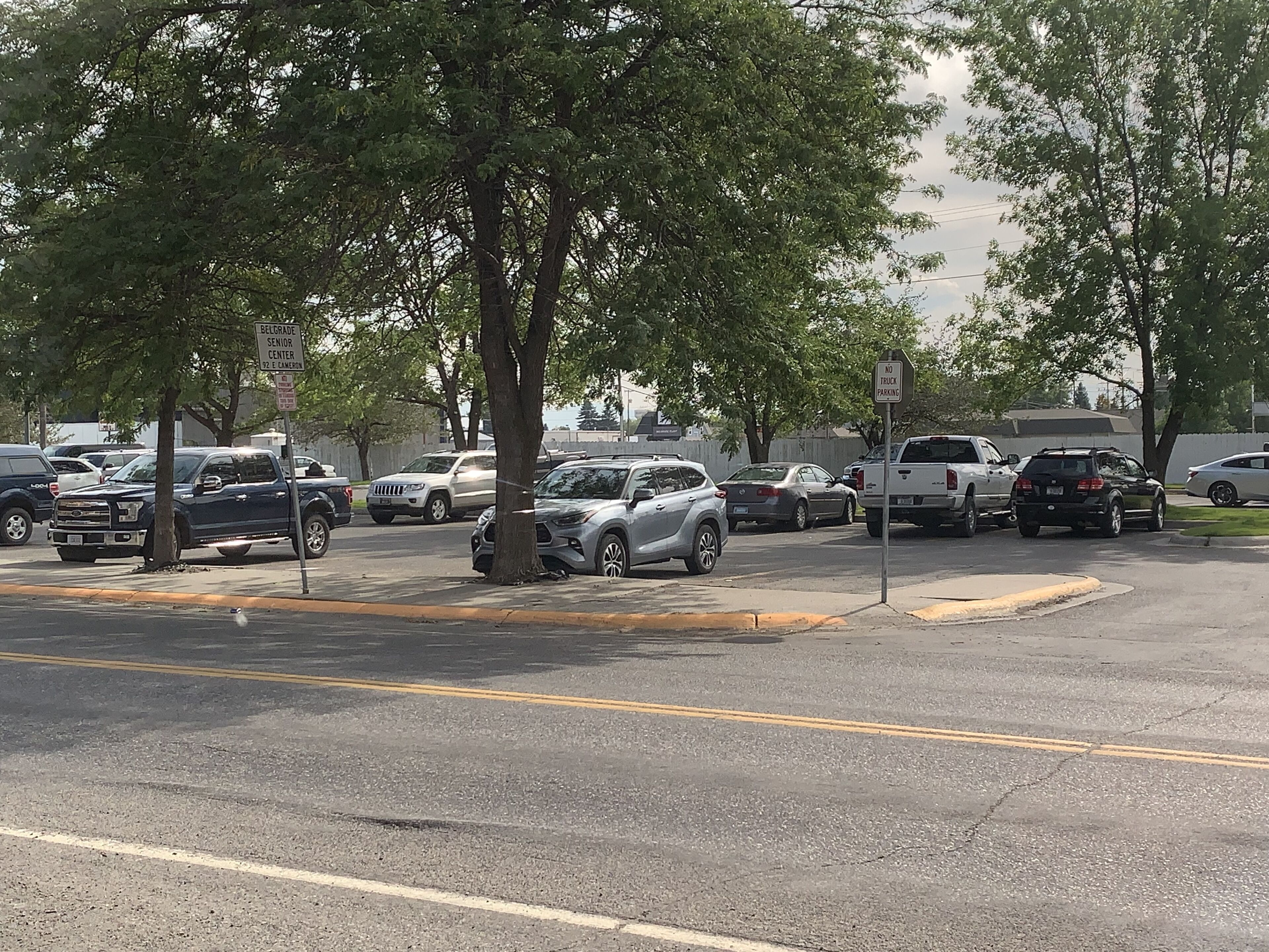 A parking lot with multiple vehicles, including cars and trucks, parked along the roadside.